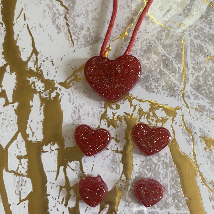 Red glitter heart-shaped set featuring one large pendant and four smaller charms on a marbled gold background.