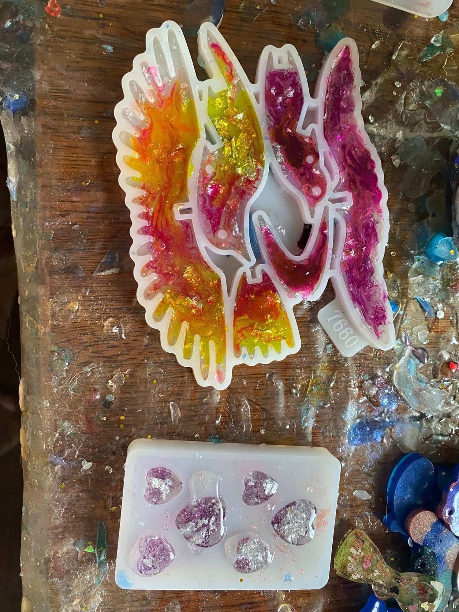 Colorful resin molds shaped like birds in flight and hearts, placed on a textured wooden surface.