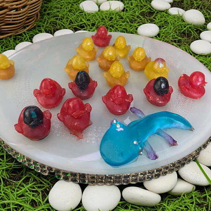 Colorful resin ducks in various shades on a round white platter, surrounded by green grass and white stones.