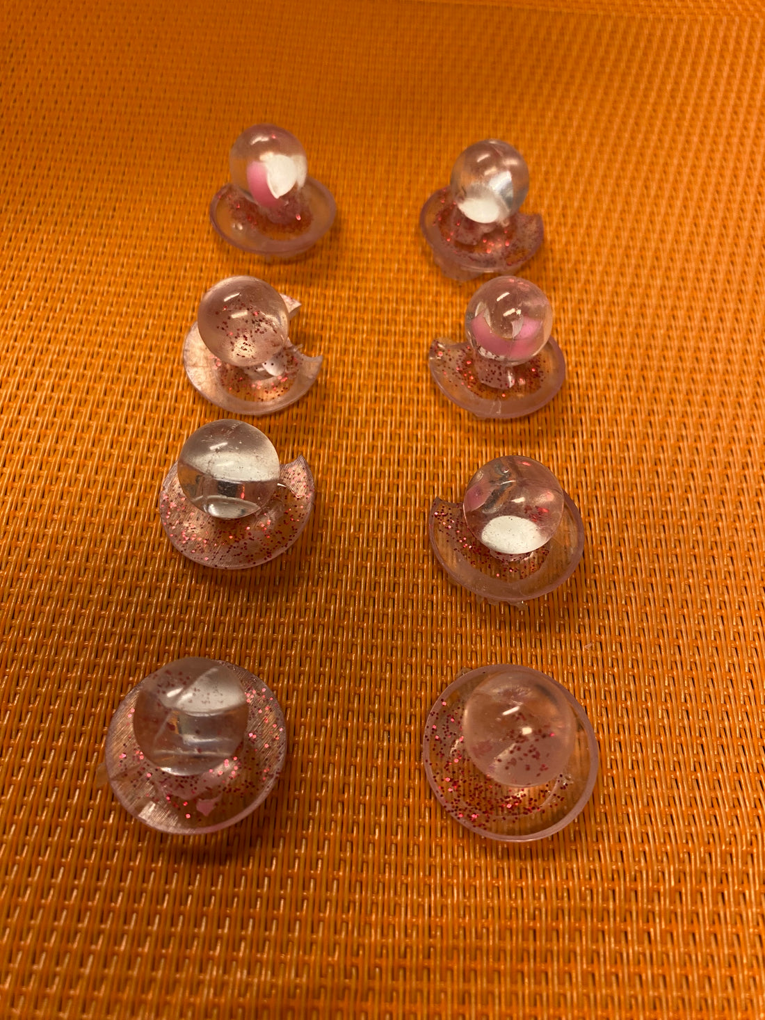 Unique chef buttons in pink and clear resin, arranged in two rows on an orange textured background.