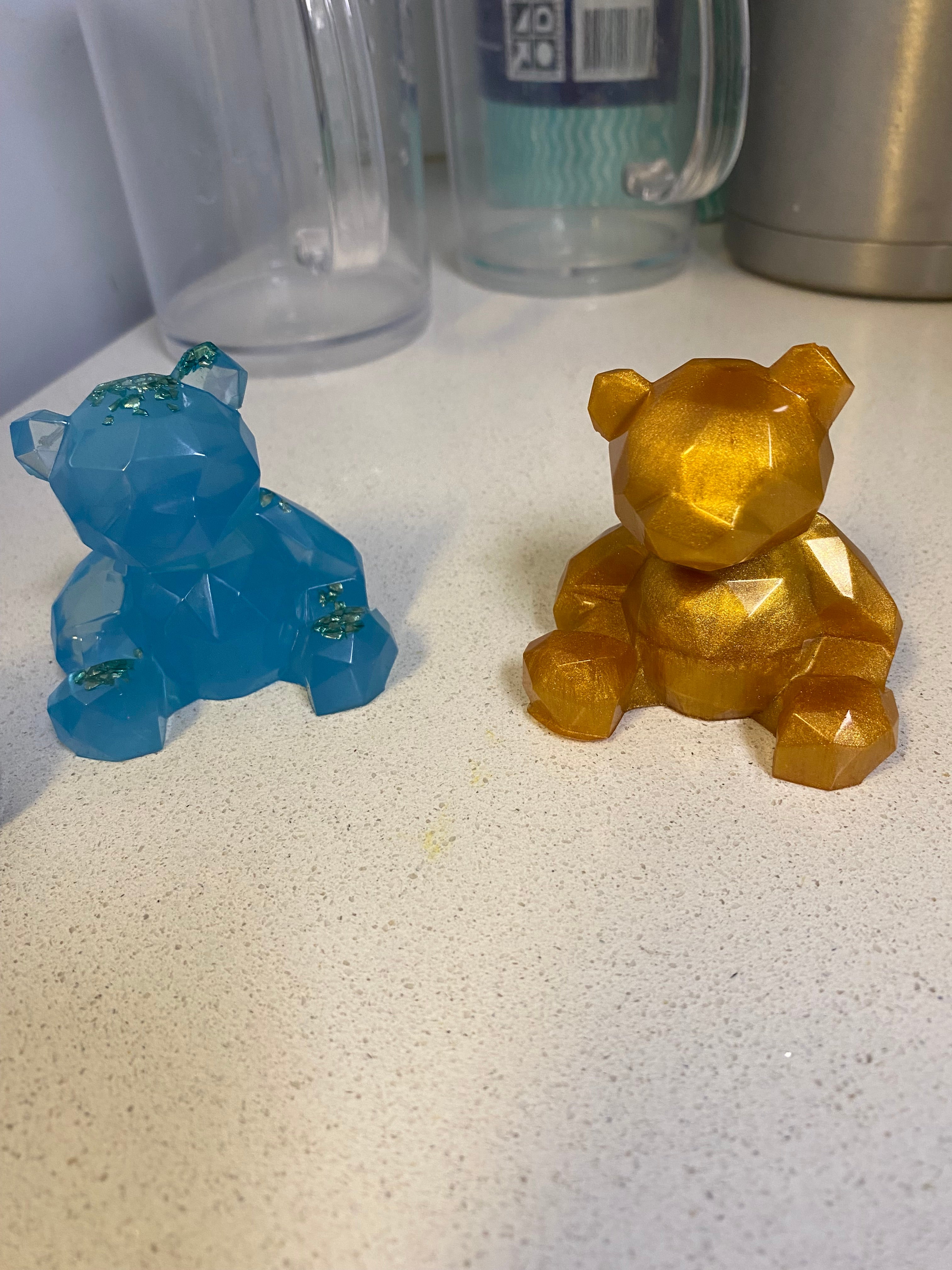 Two geometric bear figurines, one in blue and the other in gold, sitting on a white countertop.