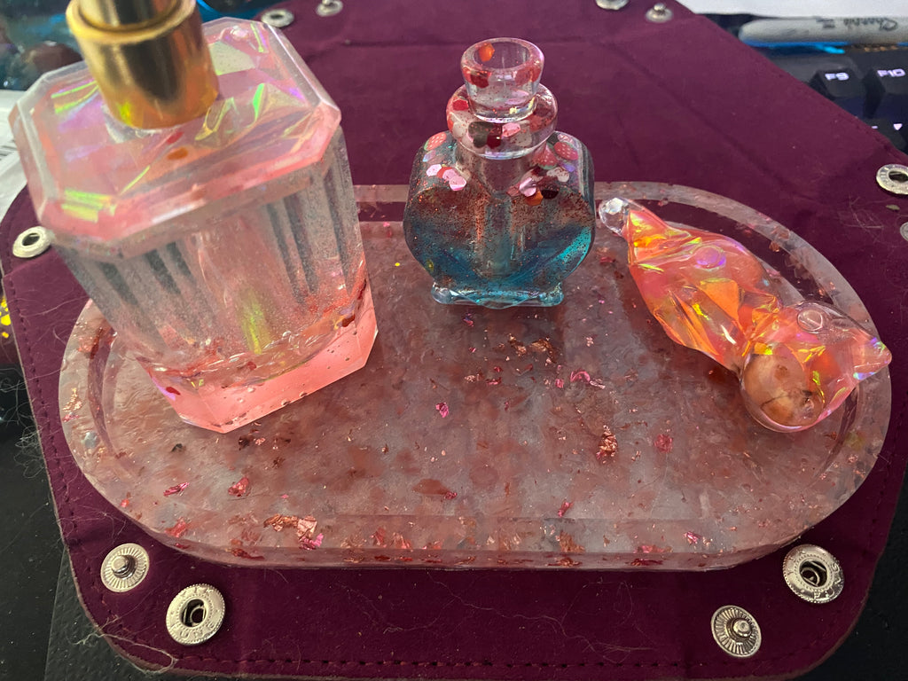 Bathroom set featuring three decorative glass bottles on a textured tray, with pink, blue, and orange hues.