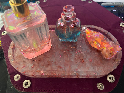 Bathroom set featuring three decorative glass bottles on a textured tray, with pink, blue, and orange hues.