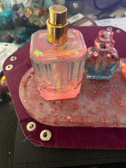 Colorful bathroom set featuring a hexagonal pink perfume bottle and a small heart-shaped blue container on a textured tray.