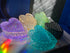 Heart-shaped trinket boxes in purple, amber, green, black, and blue arranged on a reflective surface with light reflections.
