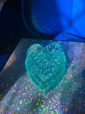 Heart-shaped trinket box in translucent teal with a textured surface, placed on a holographic background.