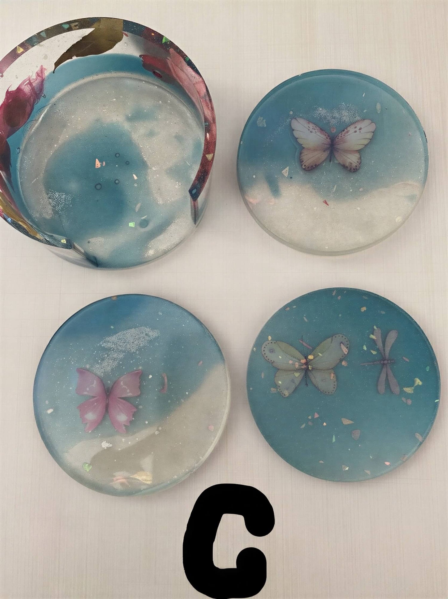 Coaster set featuring four round coasters with butterfly designs in blue and white resin.