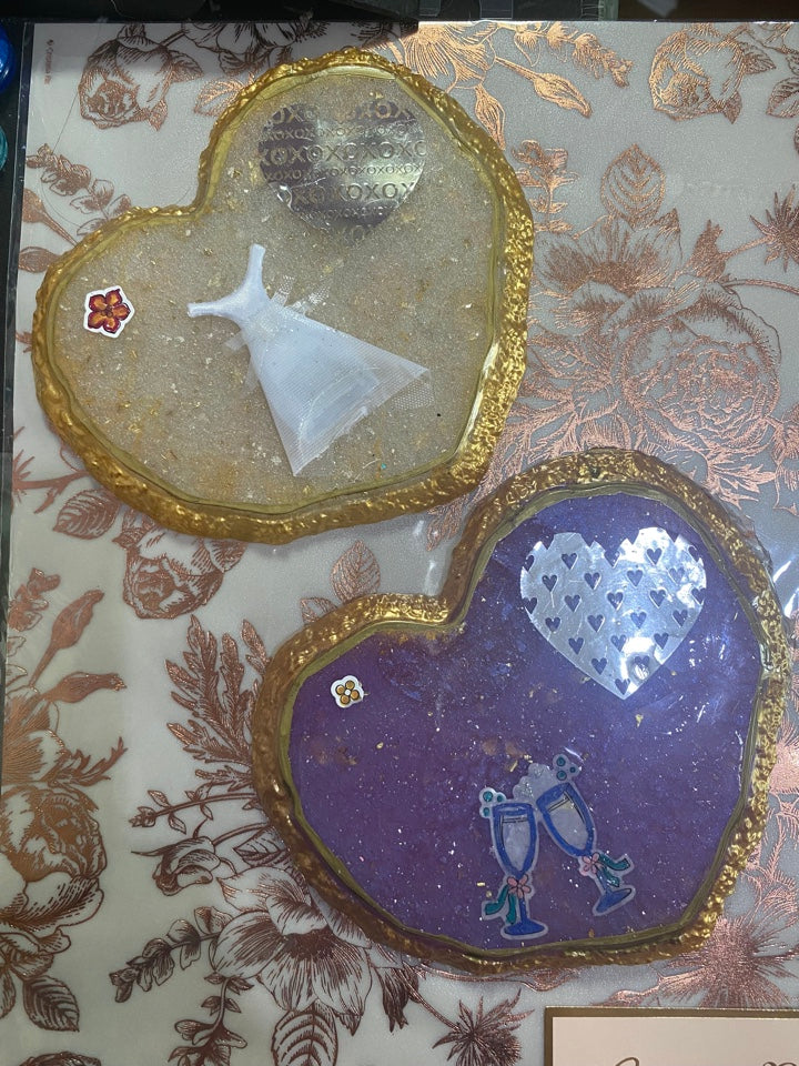 Heart-shaped wedding coasters in gold trim, featuring a wedding dress and champagne glasses on a floral background.