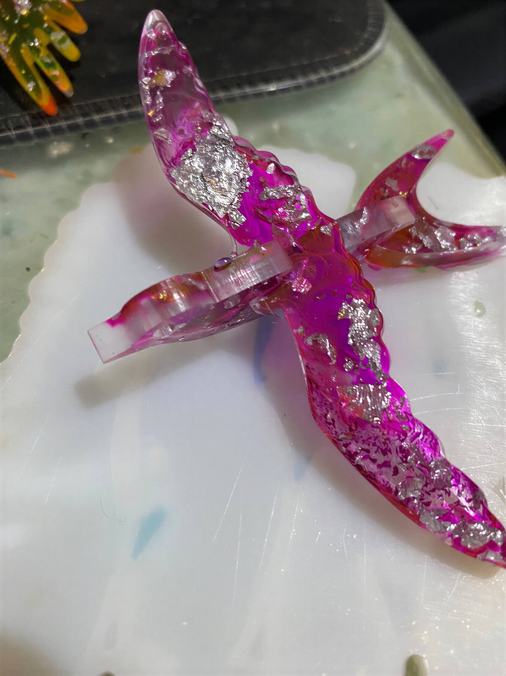 Translucent pink bird sculpture with silver accents, positioned on a white surface.
