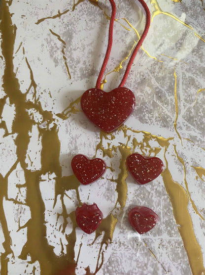 Red heart-shaped jewelry set with a larger pendant and four smaller charms, featuring a glittery finish on a gold marbled ...