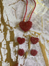 Red heart-shaped jewelry set with a larger pendant and four smaller charms, featuring a glittery finish on a gold marbled ...