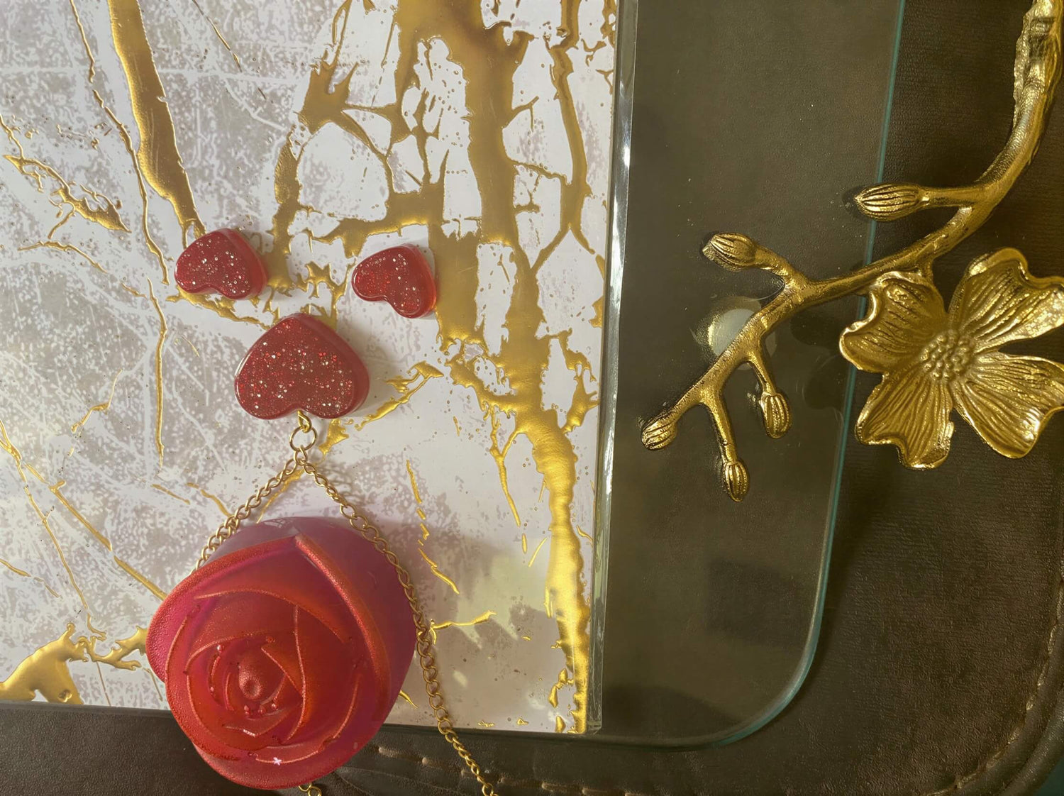 Heart-shaped red glitter earrings and a rose pendant on a textured gold and white background.