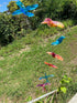 Colorful bird wind chime with six translucent birds hanging in a garden setting.