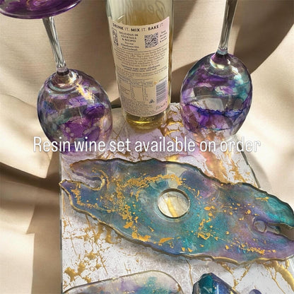 Two purple and teal resin wine glasses and a matching tray with gold flakes next to a glass bottle.