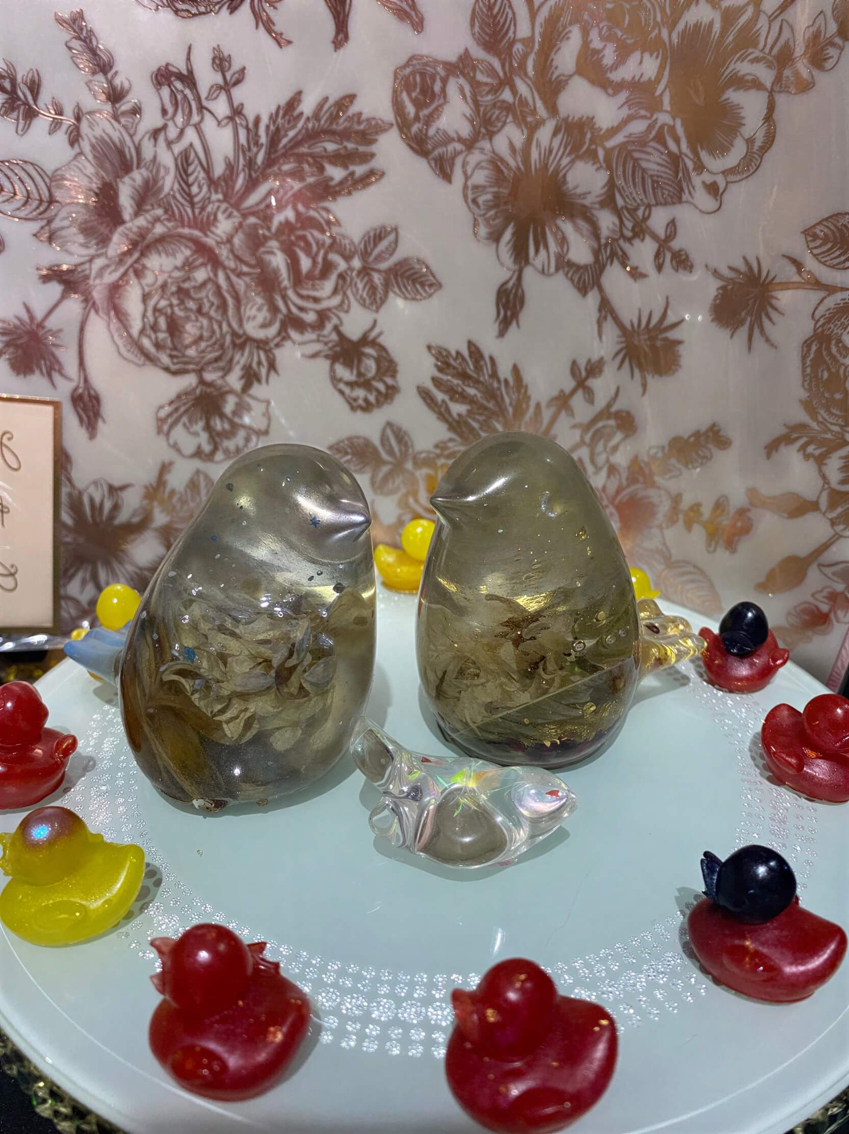 Two resin birds filled with dried flowers, positioned on a decorative plate surrounded by colorful candy shapes.