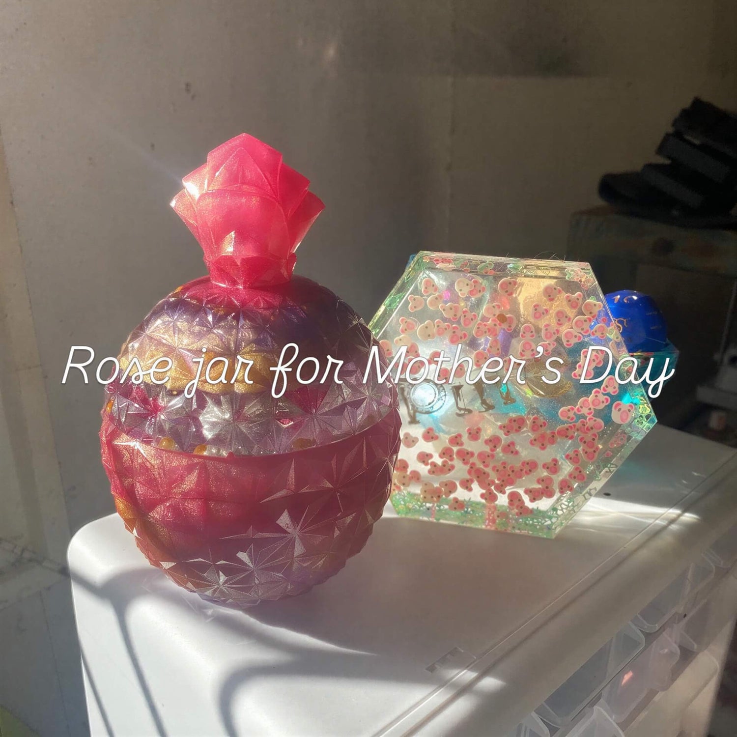 Large jar with a rose design, featuring a pink top and textured surface, placed beside a hexagonal resin jar.