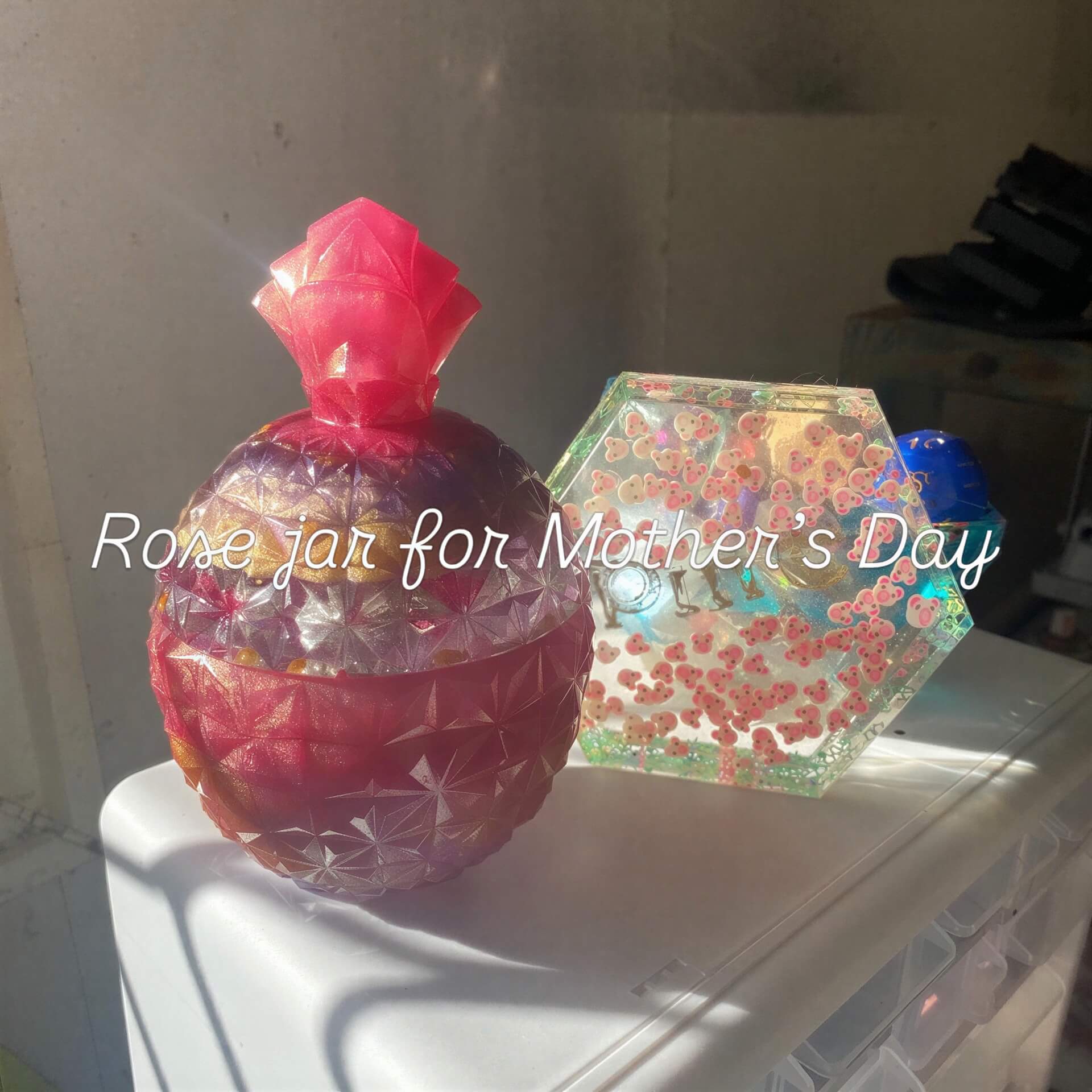 Large jar with a rose design, featuring a pink top and textured surface, placed beside a hexagonal resin jar.