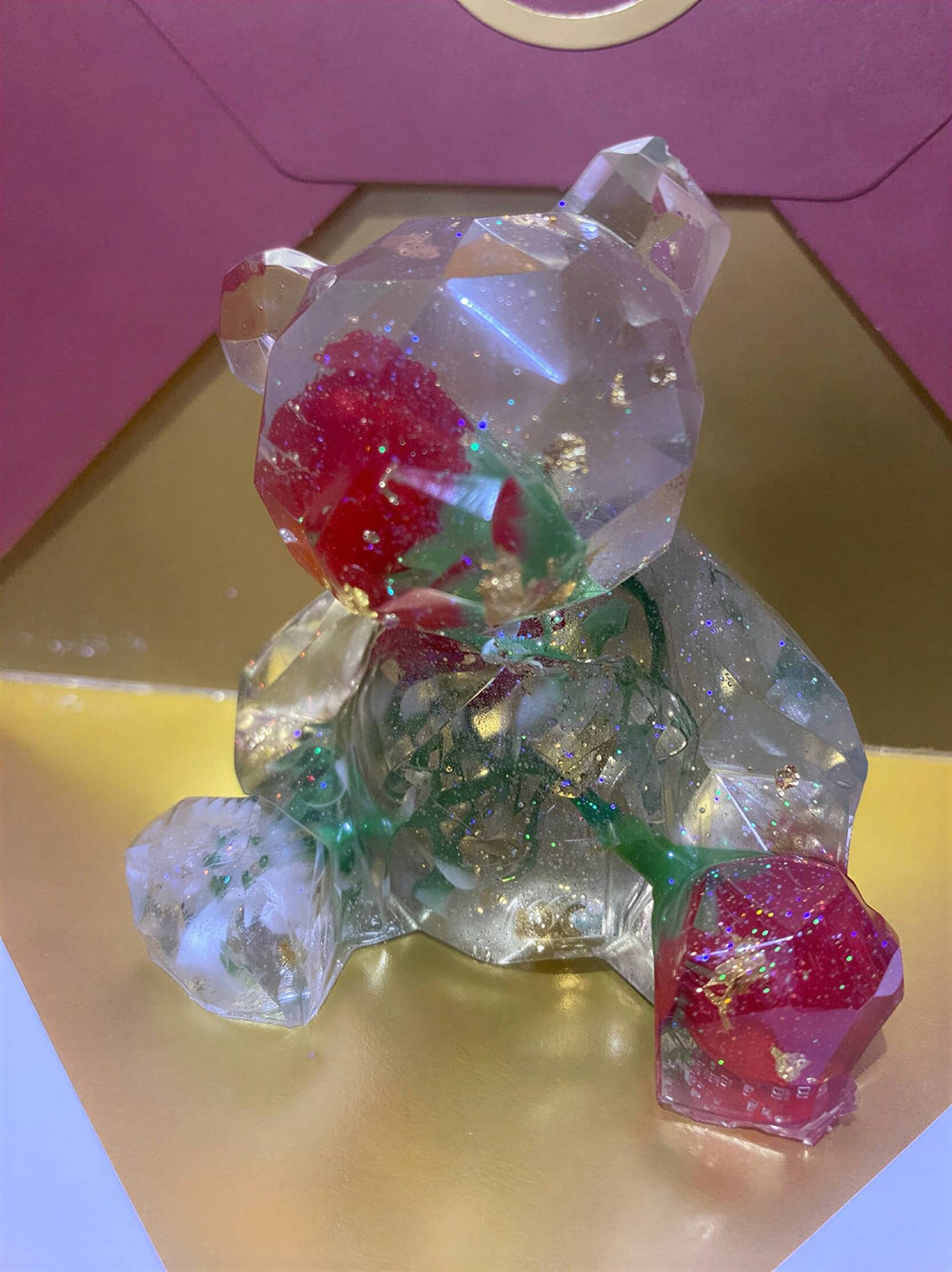 Crystal bear figurine with red rose accents, set against a gold and pink background.